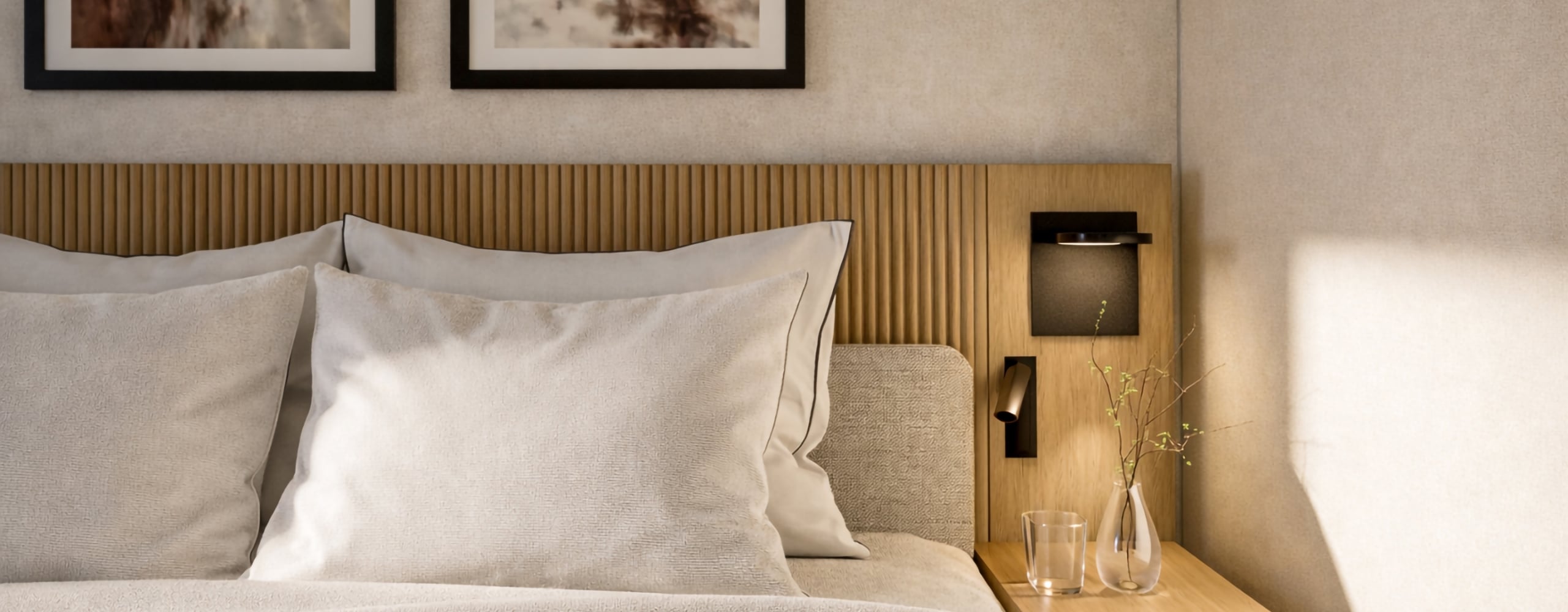 A neatly made bed with light pillows and blankets features a wooden headboard, abstract art, and a nightstand with a glass and vase, within a sunlit, modern bedroom.