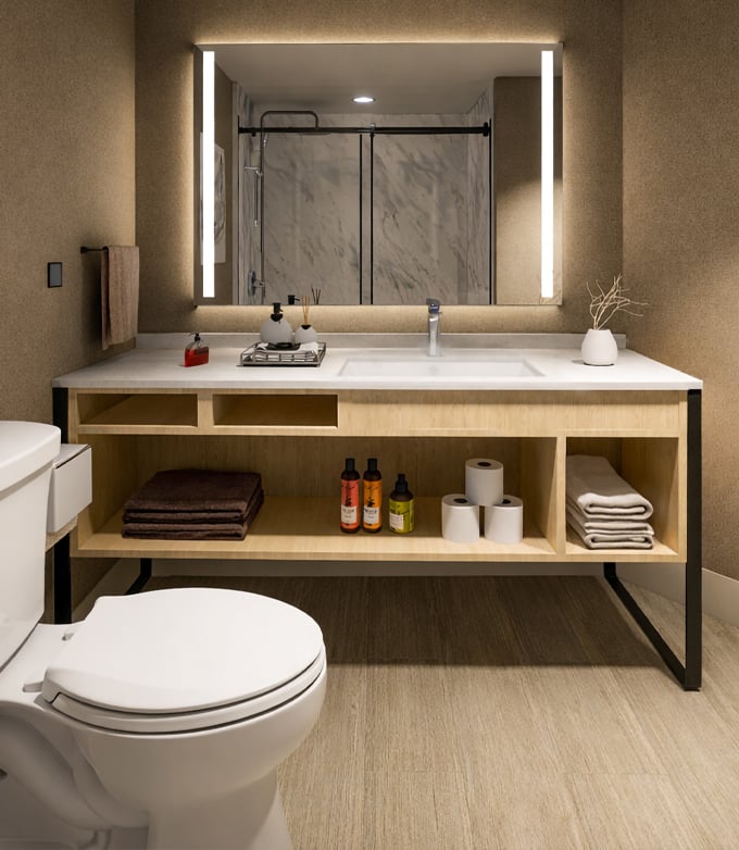 A modern vanity with a white sink and illuminated mirror displays bath products and towels. The mirror reflects a marble shower. A white toilet is visible in this clean bathroom.