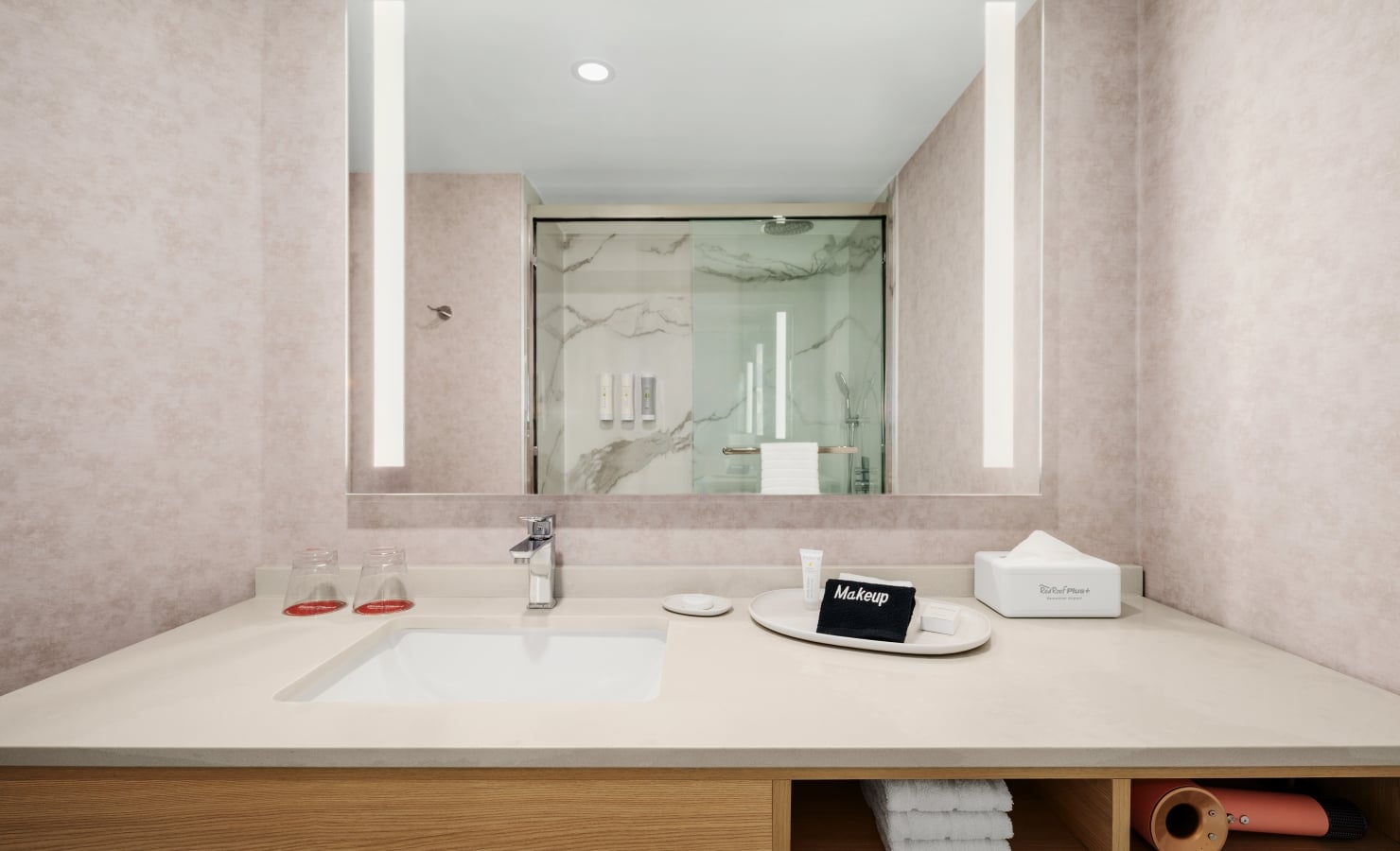 Bathroom vanity with beige walls, large mirror, and sink; toiletries and towels neatly arranged on the counter.