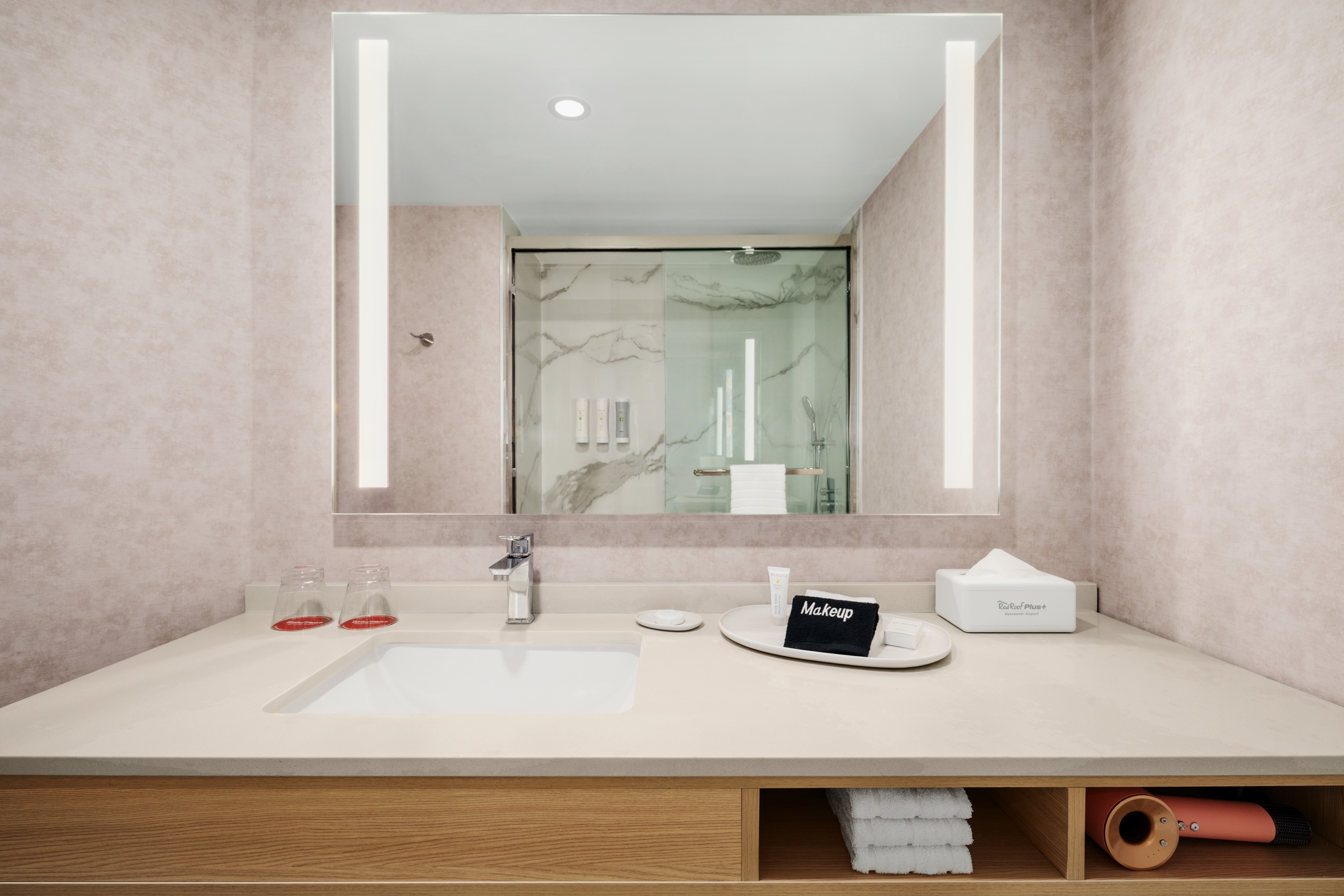 Bathroom vanity with beige walls, large mirror, and sink; toiletries and towels neatly arranged on the counter.