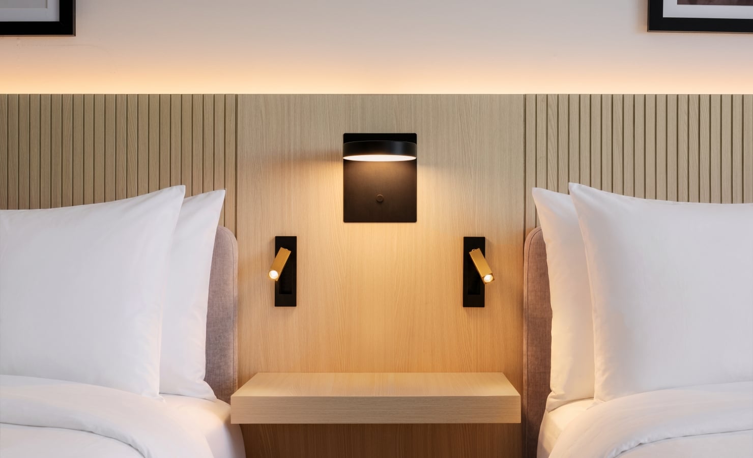 Twin beds with white pillows and a shared wooden headboard, warm wall-light between them.