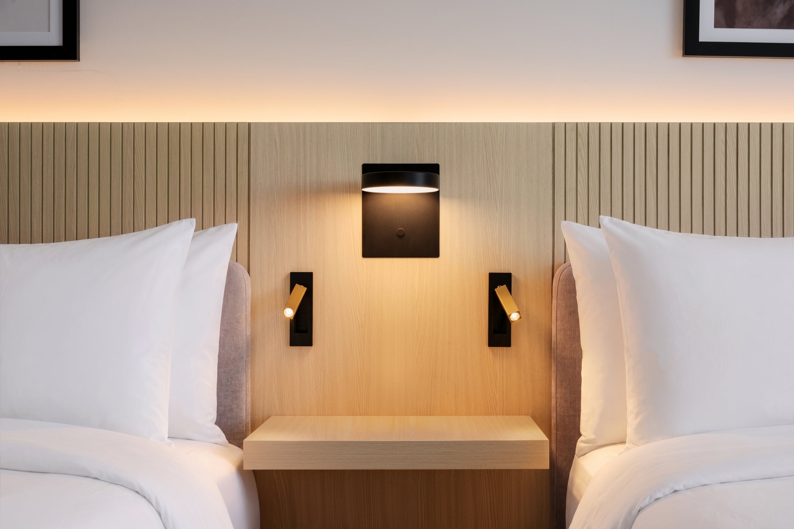 Twin beds with white pillows and a shared wooden headboard, warm wall-light between them.