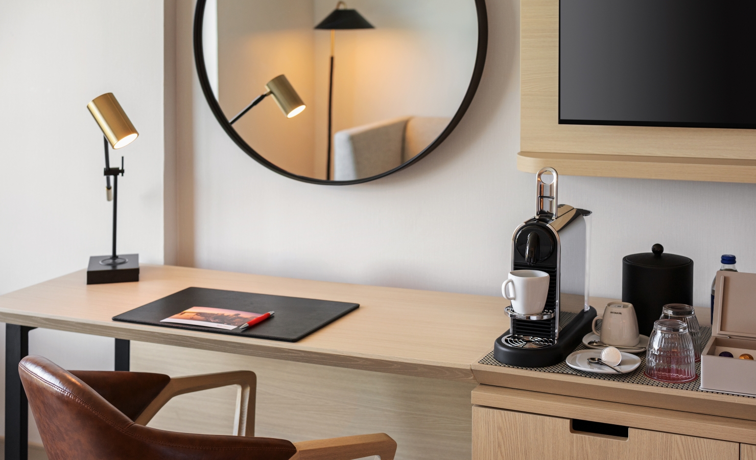 Desk setup with a circular wall mirror, gold task lamp, and a coffee station on the right side of the desk.