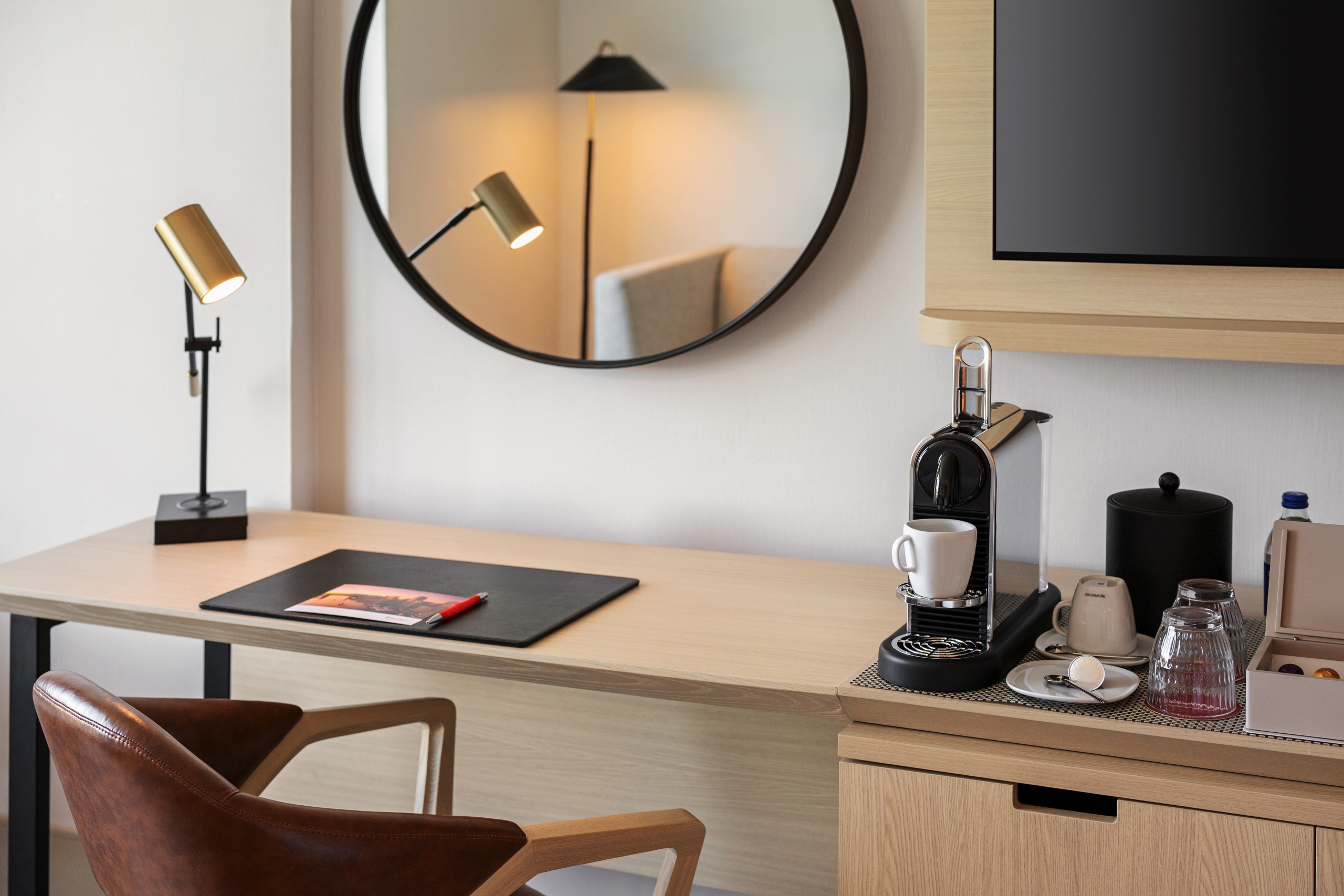 Desk setup with a circular wall mirror, gold task lamp, and a coffee station on the right side of the desk.
