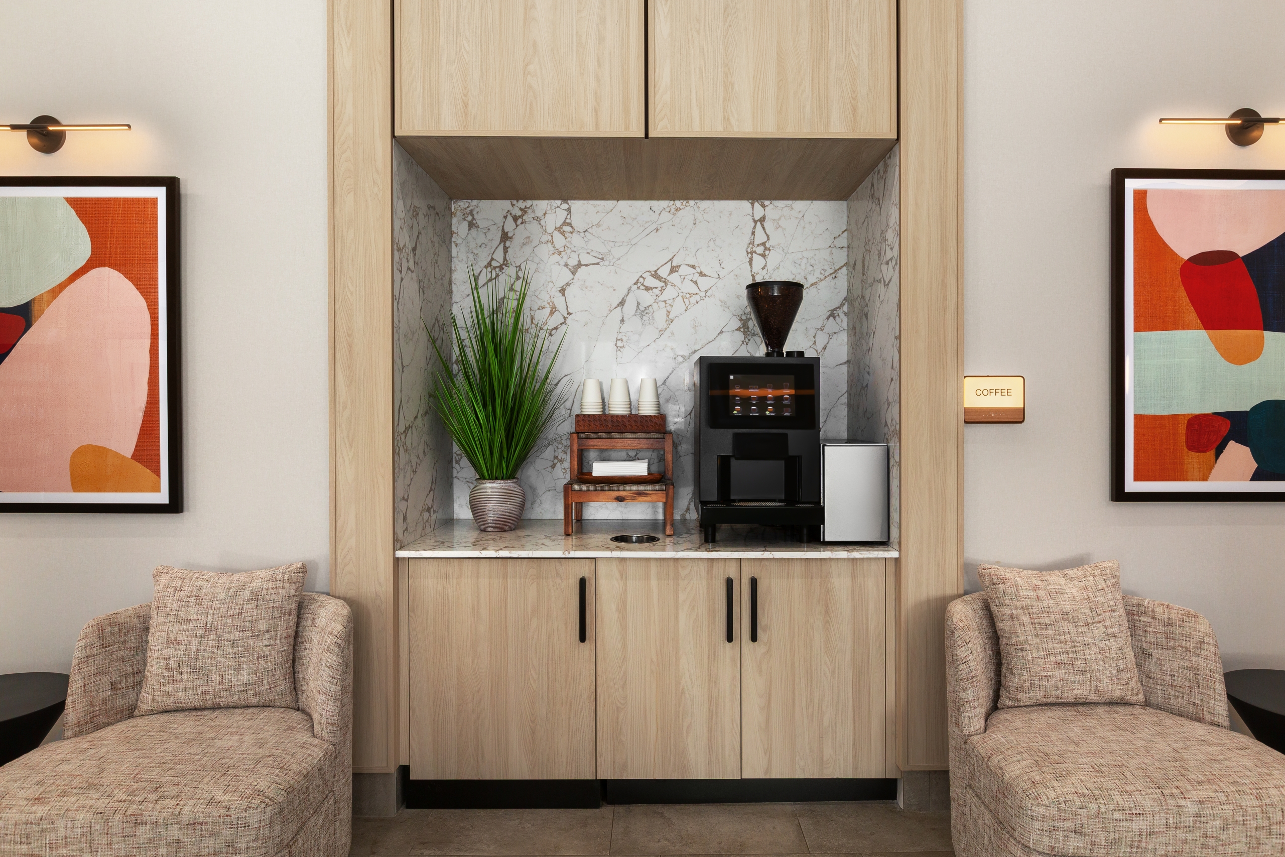 Built-in coffee bar with marble backsplash, coffee machine, grinder, cups, and a potted plant framed by wood cabinets.
