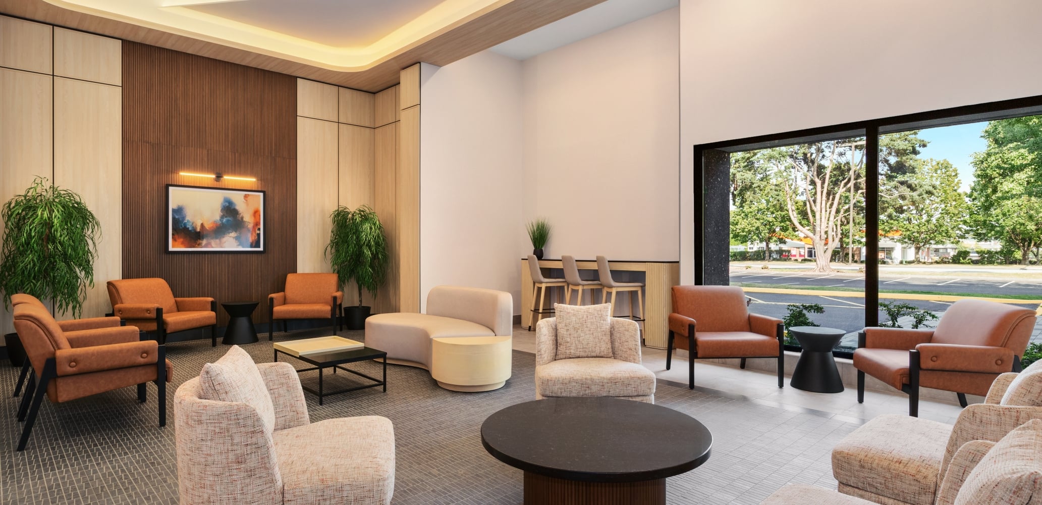 Modern hotel lobby with tan upholstered chairs, round coffee tables, and wood paneled walls near a large windowed wall.