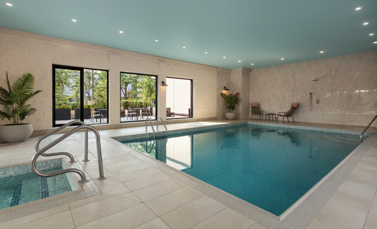 Indoor pool area with a turquoise ceiling, large windows, loungers, and potted plants beside the water.