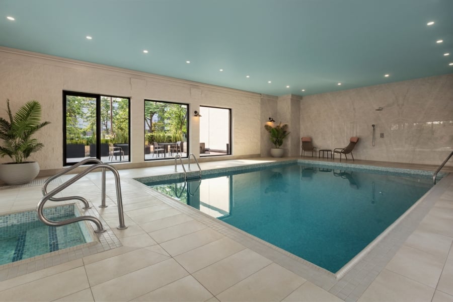 Indoor pool area with a turquoise ceiling, large windows, loungers, and potted plants beside the water.